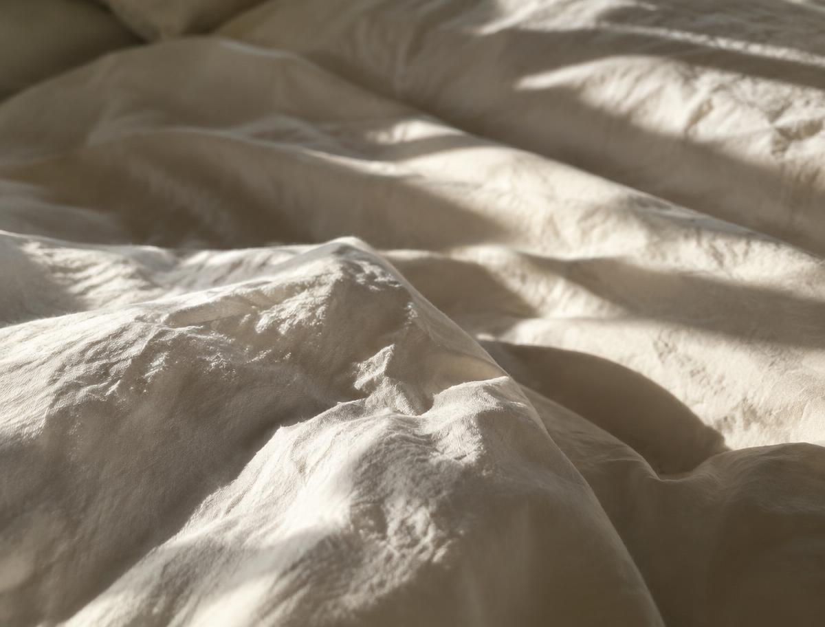 Morning light falling across crumpled white linen sheets